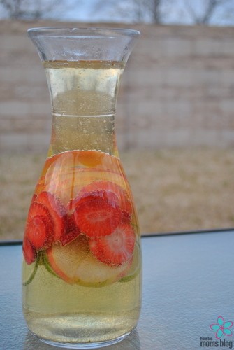 A glass pitcher filled with sangria with strawberries, apples, and limes. 