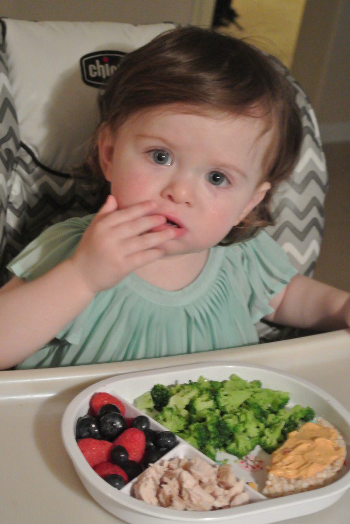 A toddler with a meal in front of her in a divided plate. 