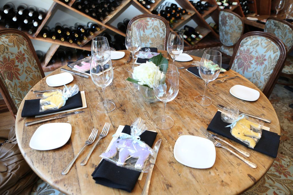 A set table. Each table setting has a different colored frosted elephant cookie wrapped in cellophane. 