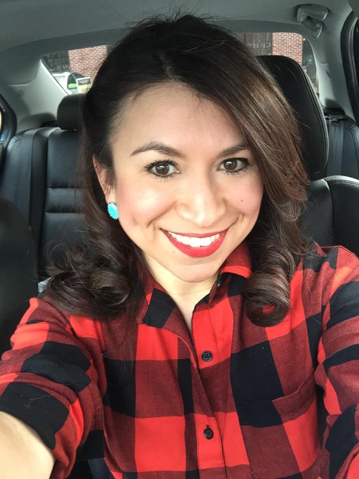 A woman with styled hair and makeup sitting in a car and taking a selfie. 