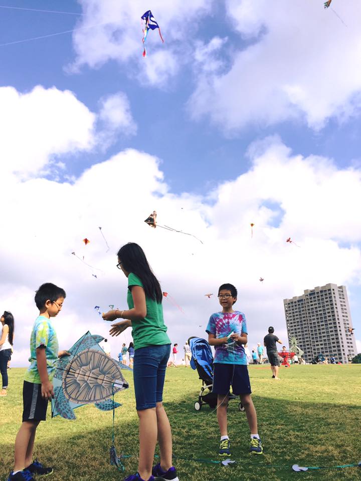 A mother and two children flying kites in a park. 