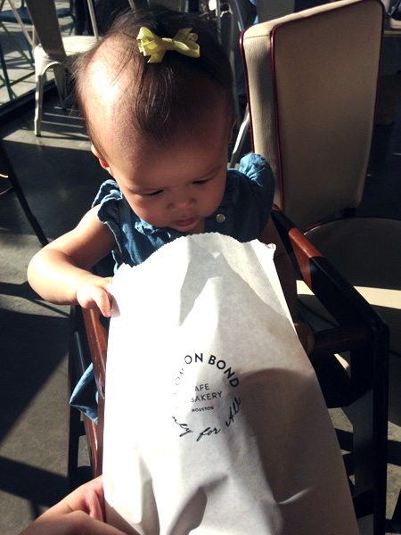 A baby looking into a bakery bag. 