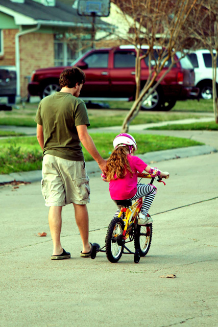 A photograph of a father helping a daughter ride a bike. 