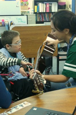 child in wheelchair works with music therapist