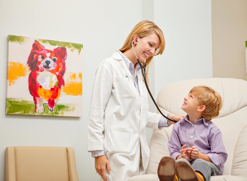 A smiling doctor holding a stethoscope to the back of a smiling boy. 