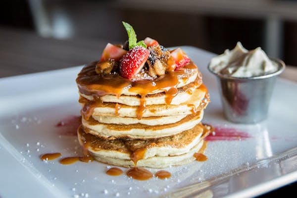 A stack of pancakes with fruit on top and whipped cream on the side.