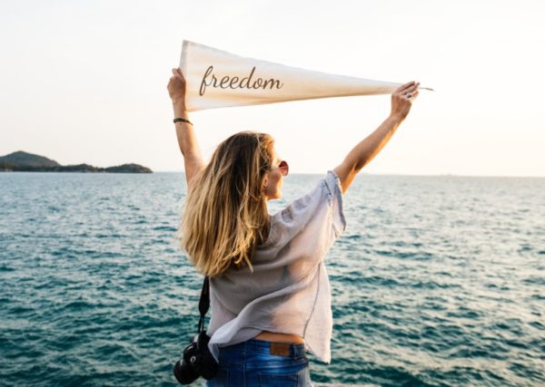 A woman facing the ocean and holding up a sign with the text Freedom.