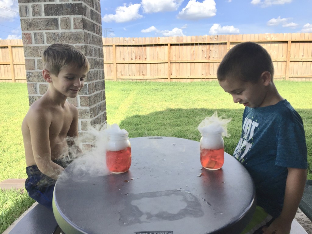 boys sit outside at table doing science experiment