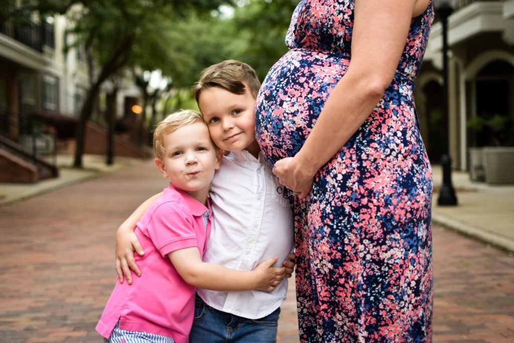Two young children with their arms wrapped around each other and their pregnant mother. 