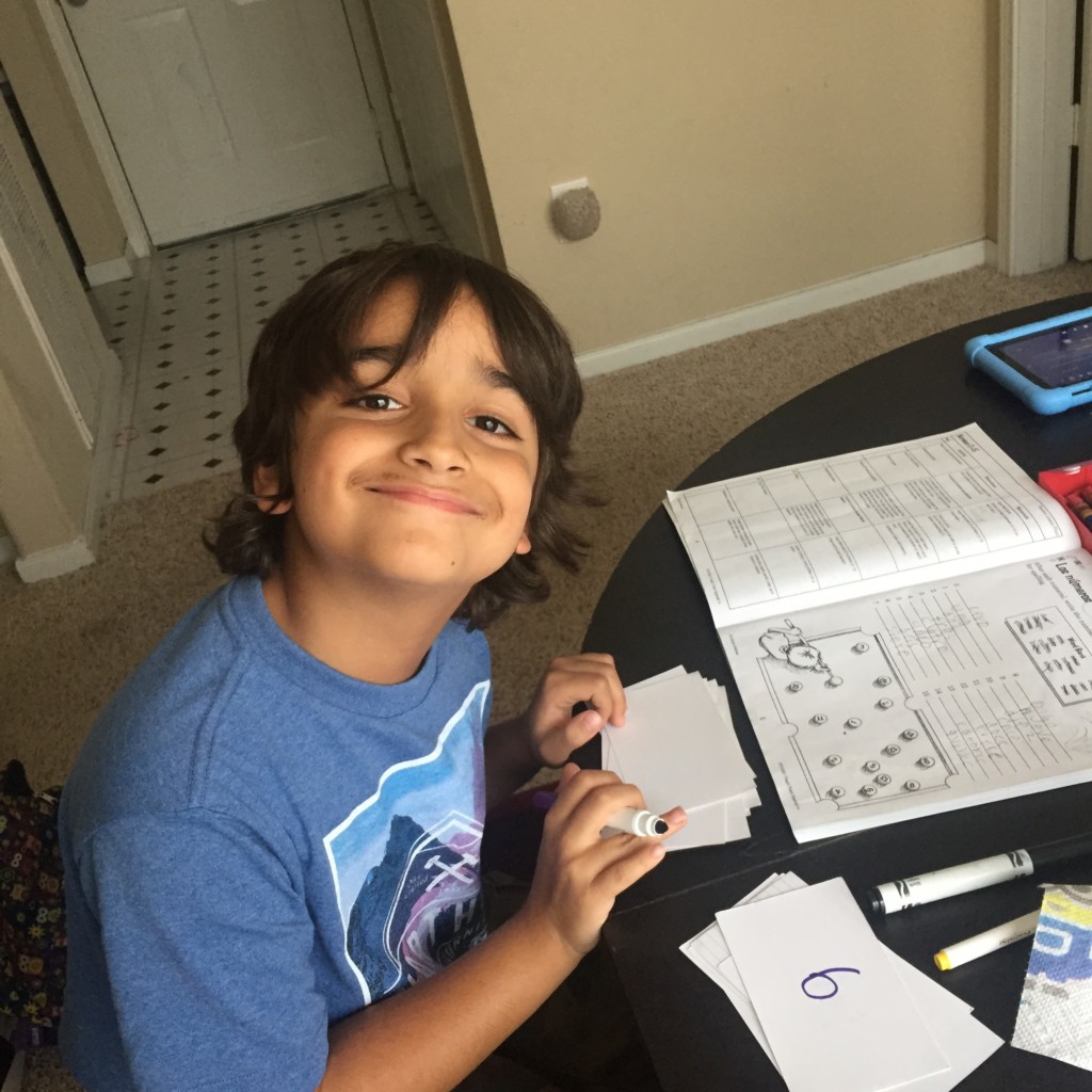 A boy smiles at the camera while making flashcards. 