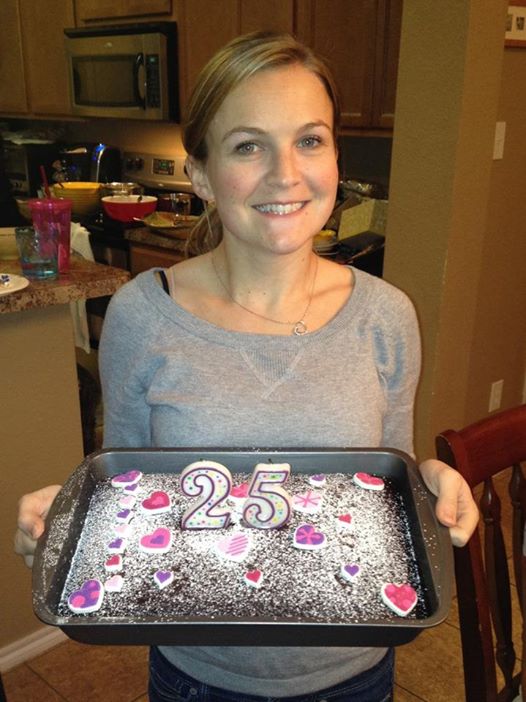 A smiling woman holding a cake with candles reading 25. 