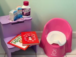 A photograph of a child's training toilet, children's books, a bottle of Miralax and two juice containers. 