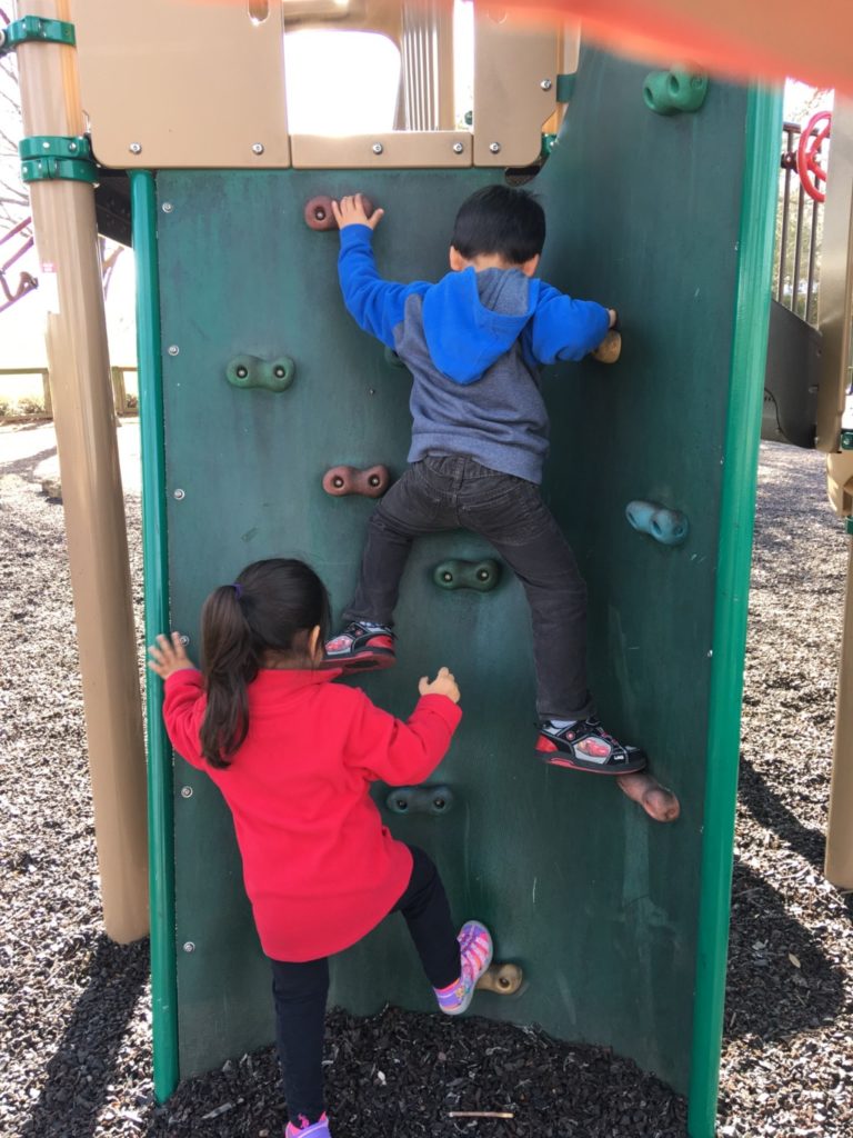 Two young children climbing a wall at a playground. 