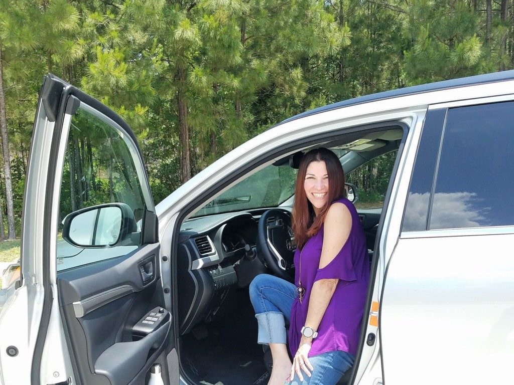 A woman smiling in the driver's seat of a car. 