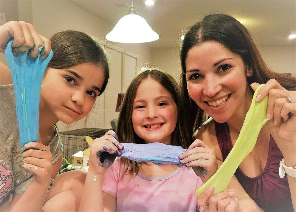 A mother and two daughters each holding a different colored slime. 