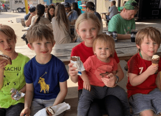 Five children sitting at a picnic bench and eating ice cream.