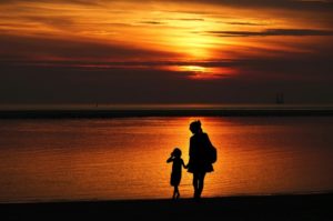 A mother and a daughter holding hands at a beach at sunset. 