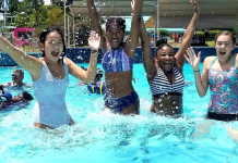 A photograph of four smiling teenage girls jumping in a pool at a waterpark