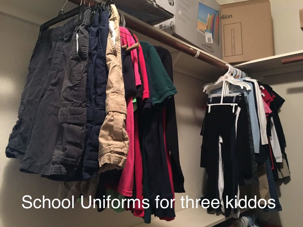 A closet with hanging clothes labeled School uniforms for three kiddos. 