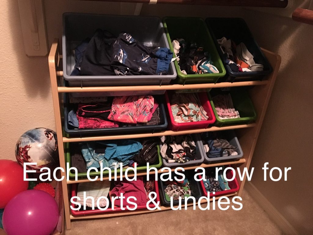 A set of plastic bins on four shelves labeled Each child has a row for shorts and undies. 