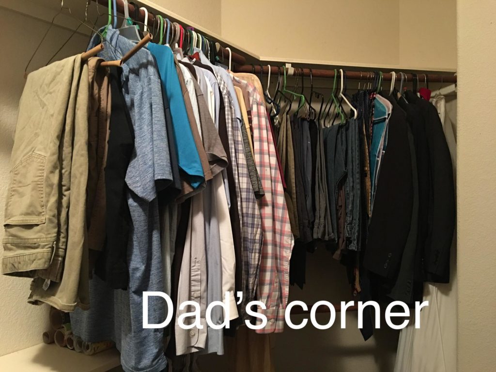 Clothes hanging in a closet labeled dad's corner. 