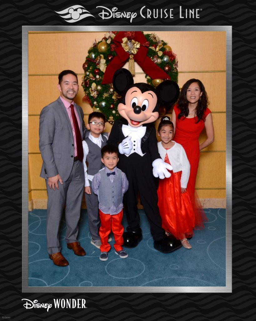 A photograph in a Disney Cruise Line frame of a mother, father and three children posing with Mickey Mouse all wearing formalwear. 