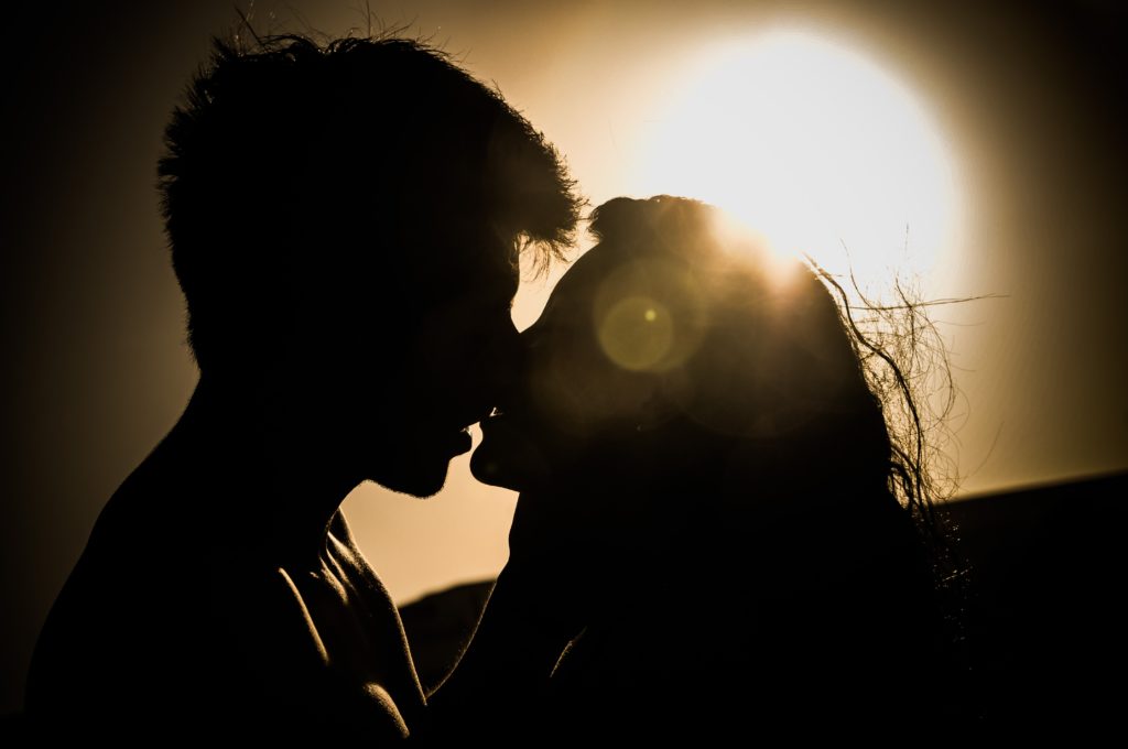 A backlit photograph of a man and woman kissing. 