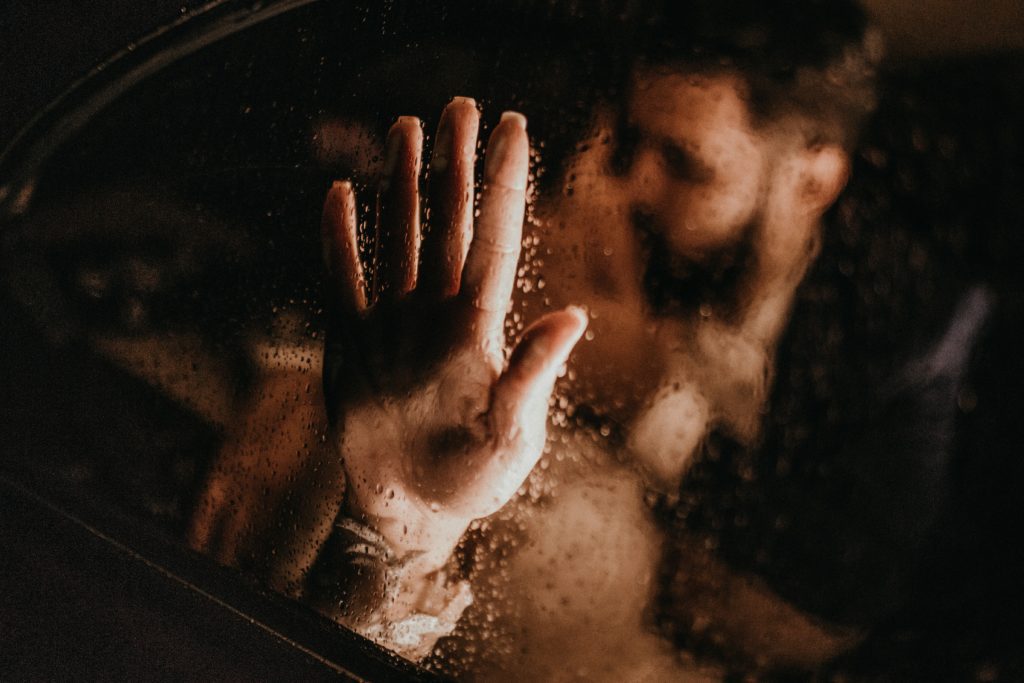 A photograph of a man and woman kissing in a car. The woman's hand is pressed against a steamy window. 