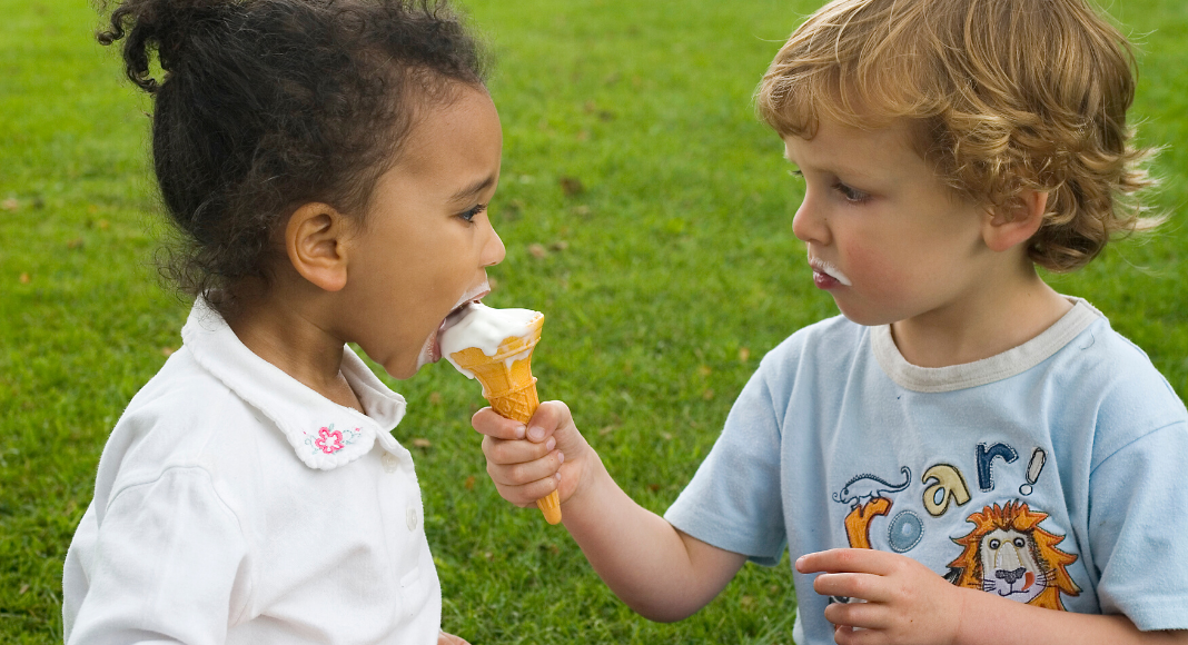 one child feeding another child an ice cream cone
