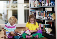 Two children sitting on a library floor and reading.