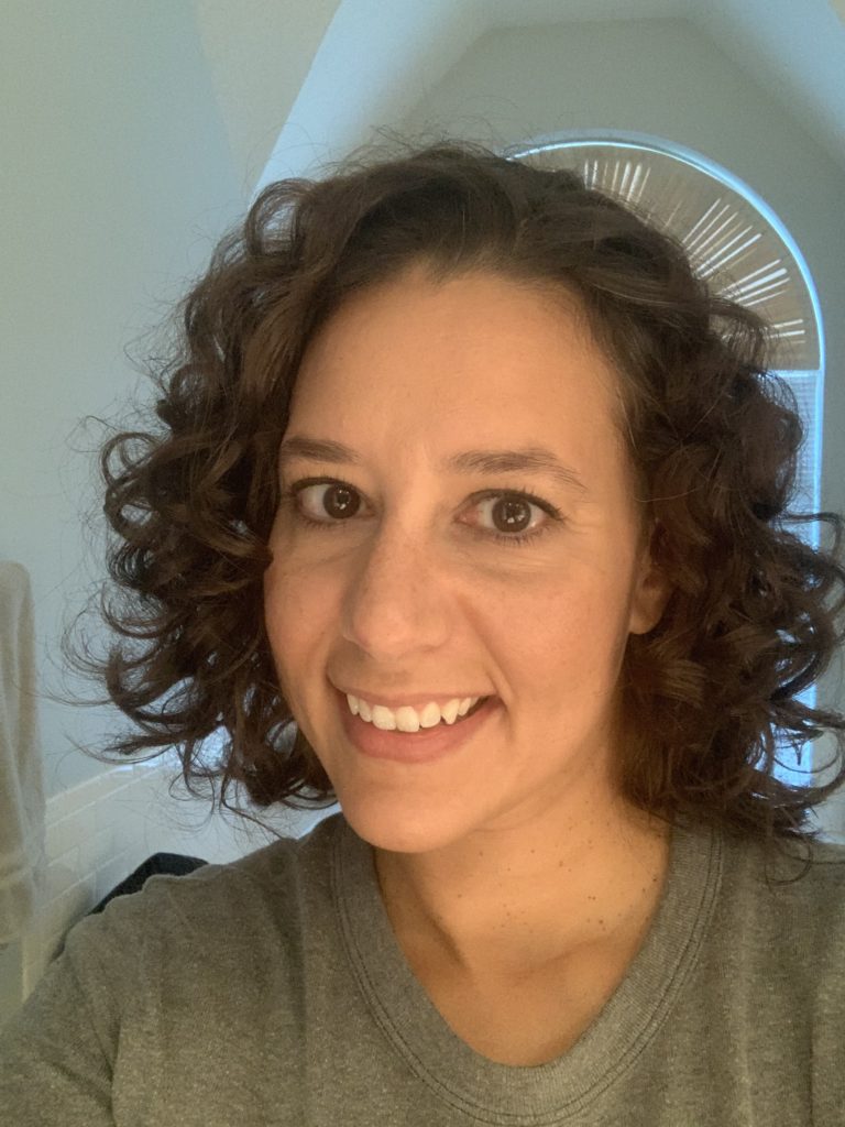 A smiling woman with curly hair to her shoulders. 