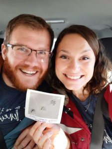 A smiling husband and wife holding up a picture of three embryos. 