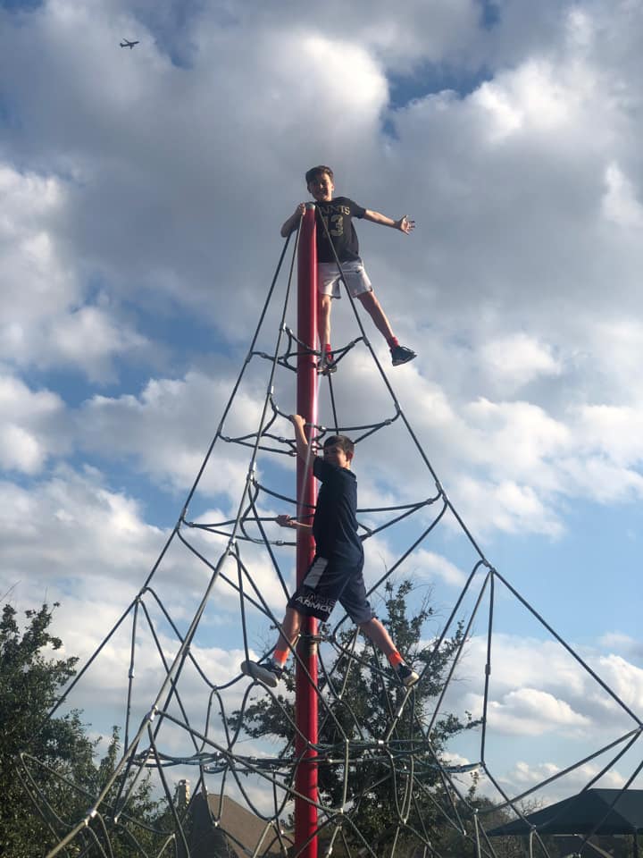 Two children climbing a metal climbing structure at a playground. 