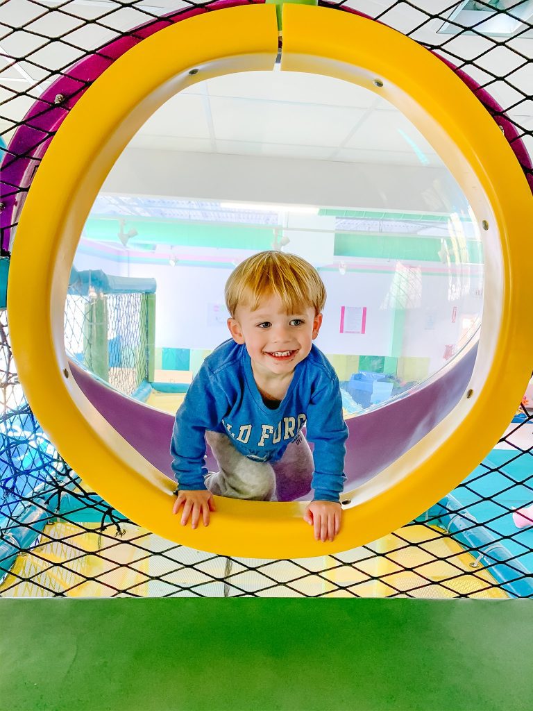 A smiling child in a tunnel at an indoor playground.