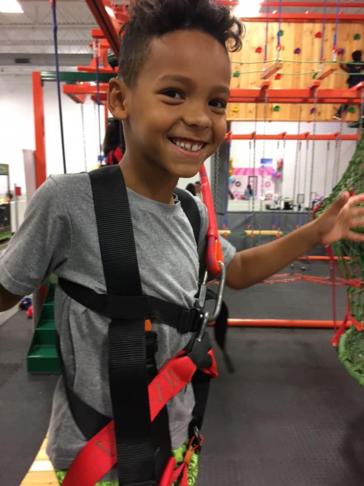 A smiling child wearing a safety harness at an indoor playground. 