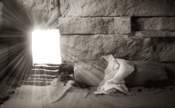 A room made of stone with light coming in a doorway and a shroud on a stone.