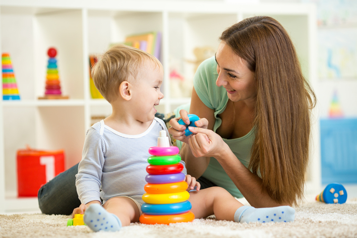 A mother playing with a toddler with a stacked ring toy. 
