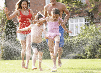 A family of four running through a sprinkler.
