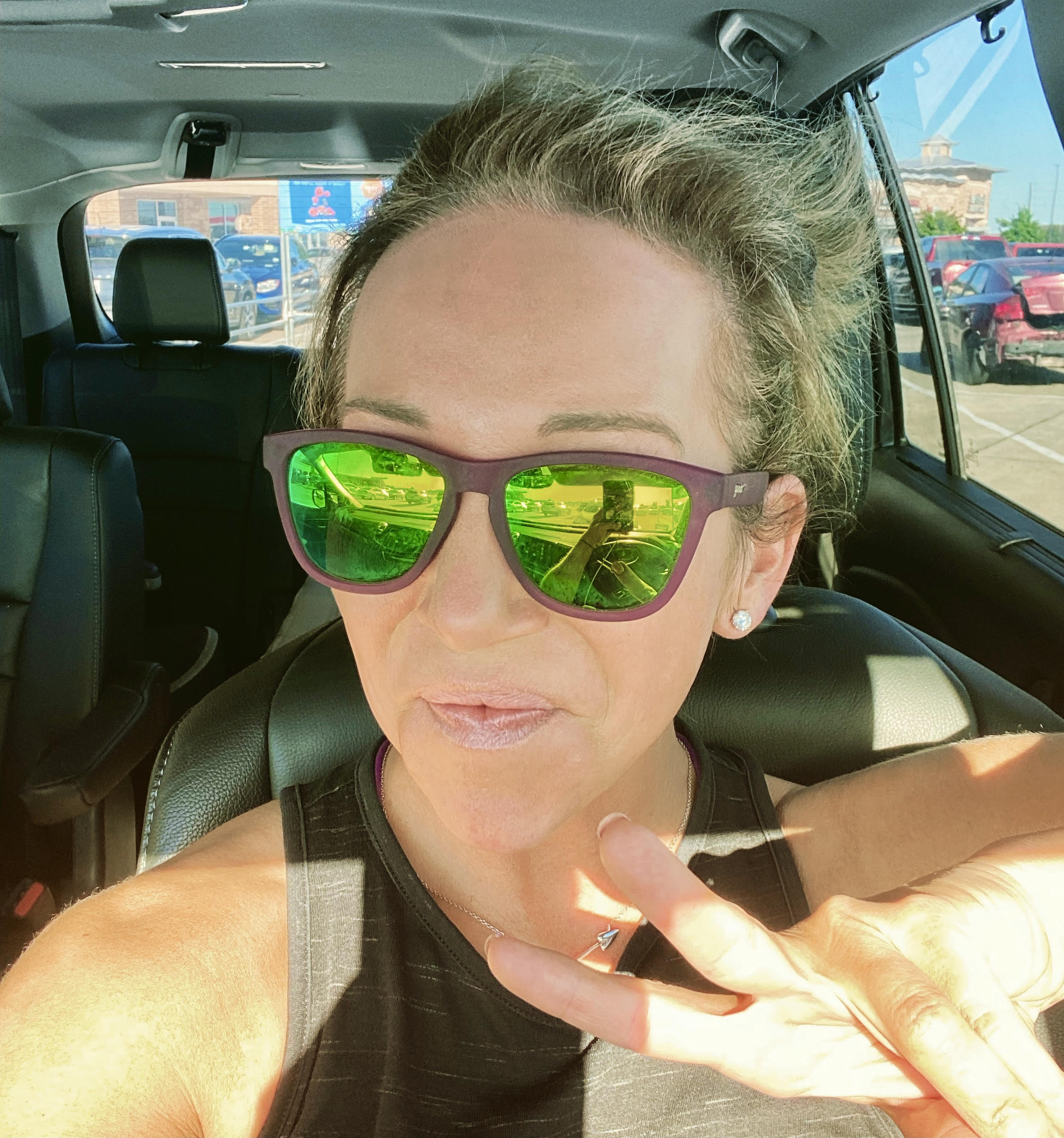 A woman with a top knot taking a selfie in the driver's seat of a car. 