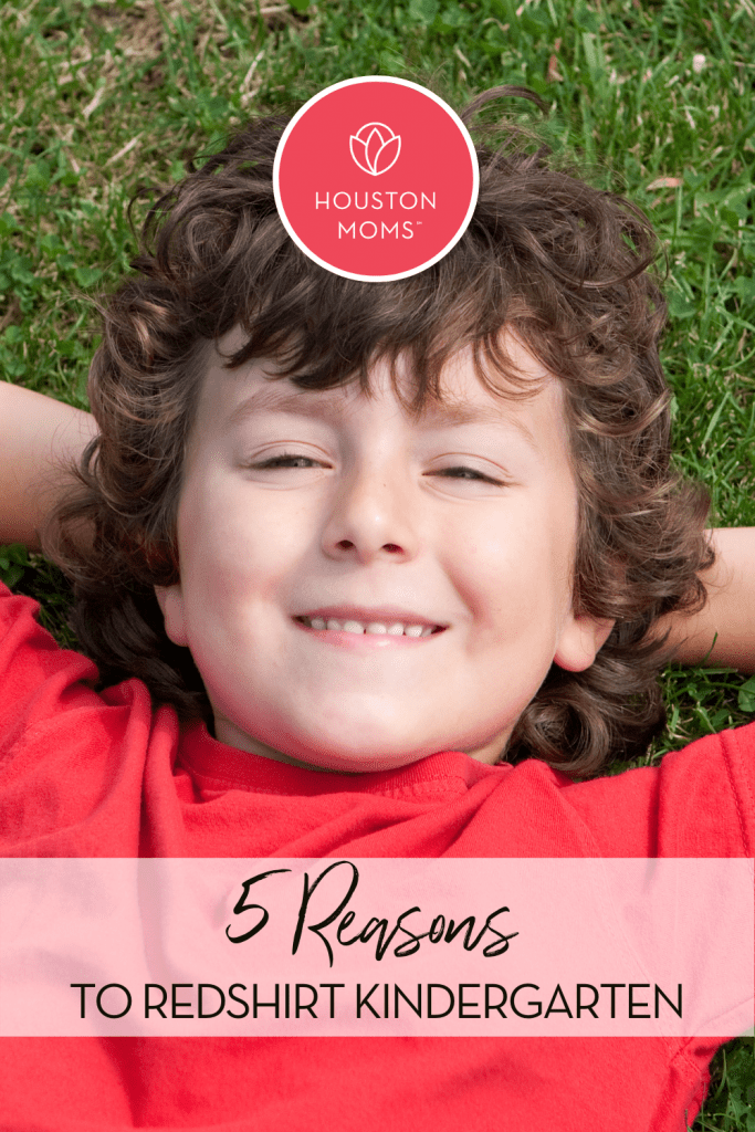 Houston Moms. 5 Reasons to redshirt kindergarten. A photograph of a smiling child lying on the grass and wearing a red shirt. 