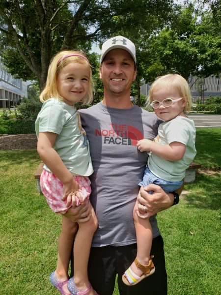 A Dad holding two daughters outside.