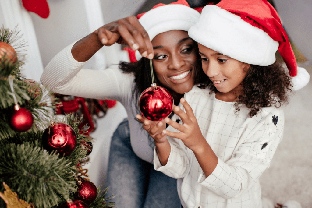 woman and girl in Santa hats admiring a red Christmas ball ornament