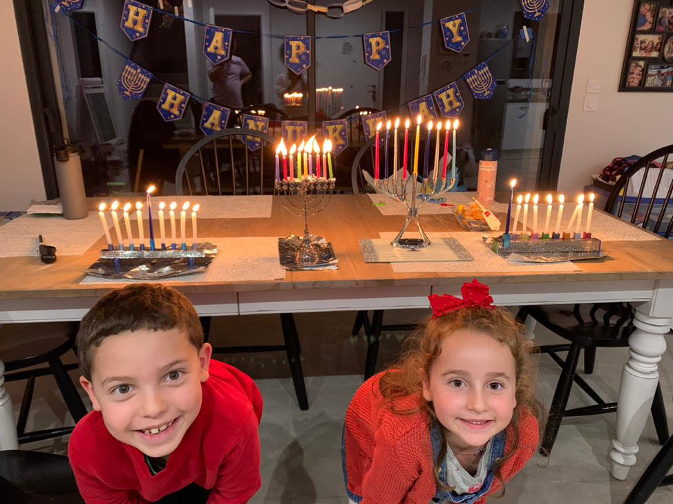 Smiling children in front of table with Hanukkah candles