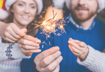 A photograph of a family of four wearing Santa hats and holding lit sparklers.