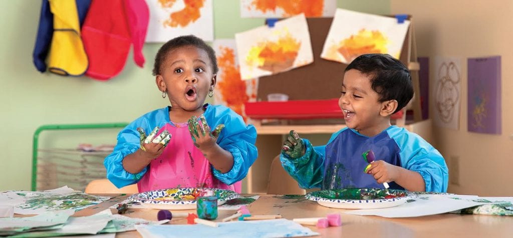 Two preschoolers laugh while their hands are covered in green paint