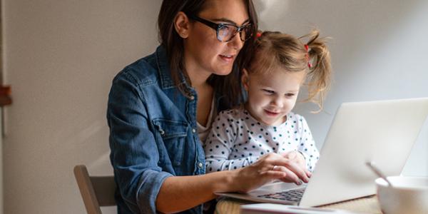 woman with little girl on her lap look at laptop