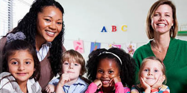 Two women and four preschoolers smile in a preschool classroom