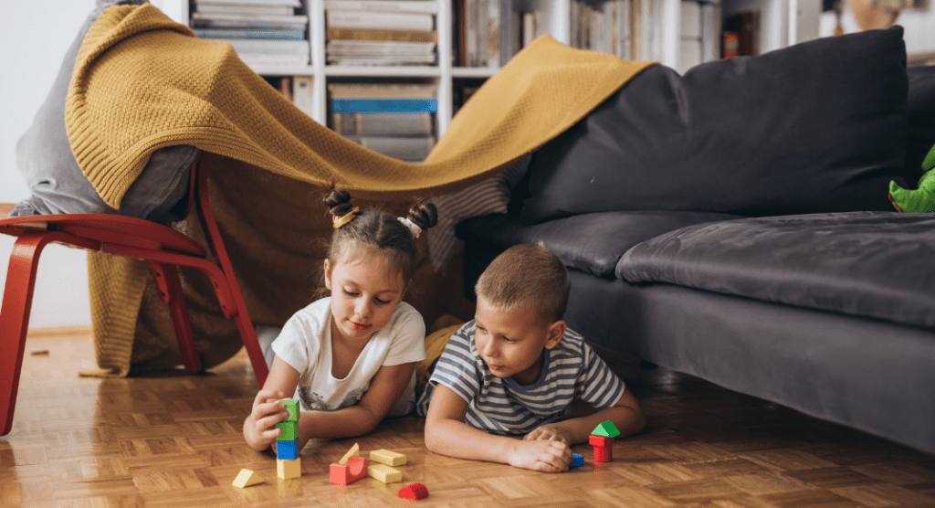 Boy and girl under a blanket fort playing with blocks