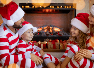 family in matching holiday pajamas sits by fire