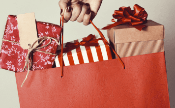 woman's hand holding a holiday shopping bag filled with wrapped gifts